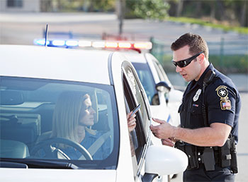 A photo of a pulled over female driver handing her license to a police officer.