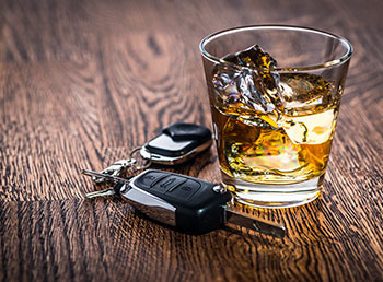 A photo of car keys next to a glass tumbler filled with liquor.