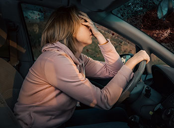 A photo of woman behind her steering wheel holding her forehead after an accident.