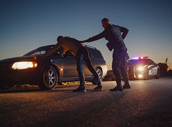 A photo of a police officer arresting a driver outside their car.